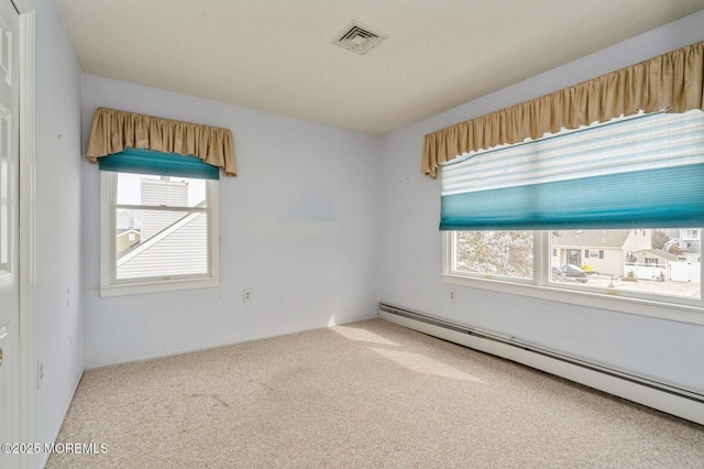 empty room featuring carpet floors, visible vents, and a baseboard heating unit