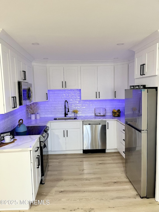 kitchen with white cabinetry, stainless steel appliances, sink, and light hardwood / wood-style flooring