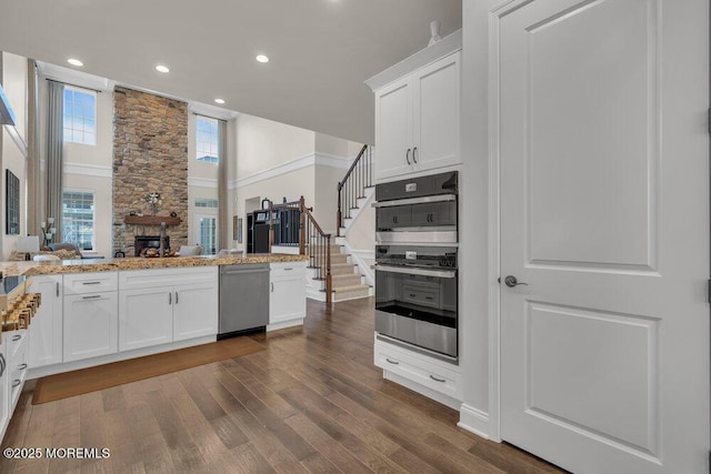 kitchen featuring open floor plan, appliances with stainless steel finishes, a peninsula, white cabinets, and dark wood-style flooring