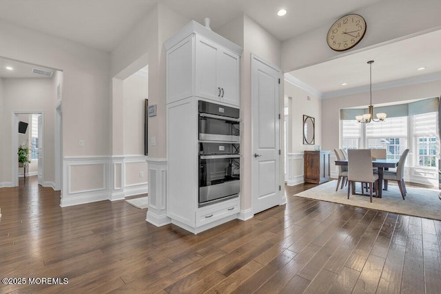 kitchen featuring stainless steel double oven, dark wood-type flooring, an inviting chandelier, and a decorative wall