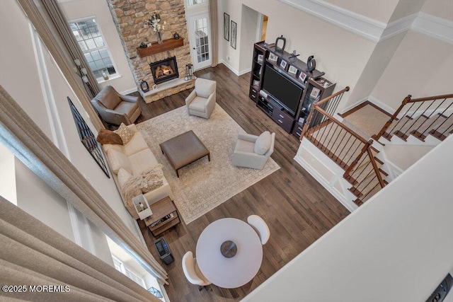 living area featuring dark wood-type flooring, a stone fireplace, baseboards, a towering ceiling, and stairs