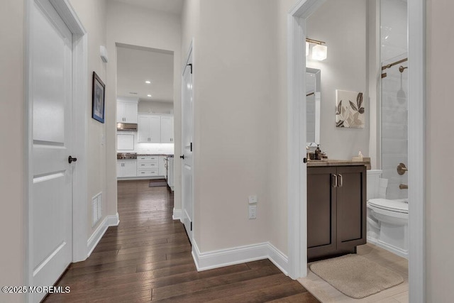 hall featuring visible vents, dark wood-type flooring, and baseboards