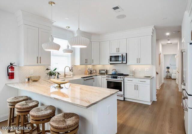 kitchen featuring hanging light fixtures, a kitchen breakfast bar, kitchen peninsula, stainless steel appliances, and white cabinets