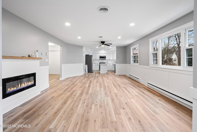 unfurnished living room featuring ceiling fan, light wood-type flooring, and a baseboard heating unit