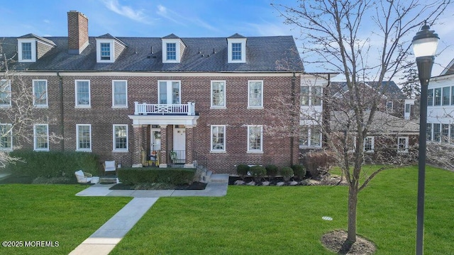 view of front of house with a chimney, brick siding, a balcony, and a front lawn