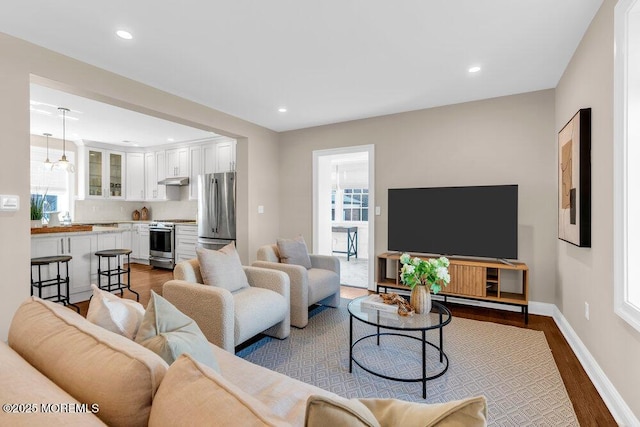 living area featuring baseboards, a healthy amount of sunlight, dark wood-style flooring, and recessed lighting