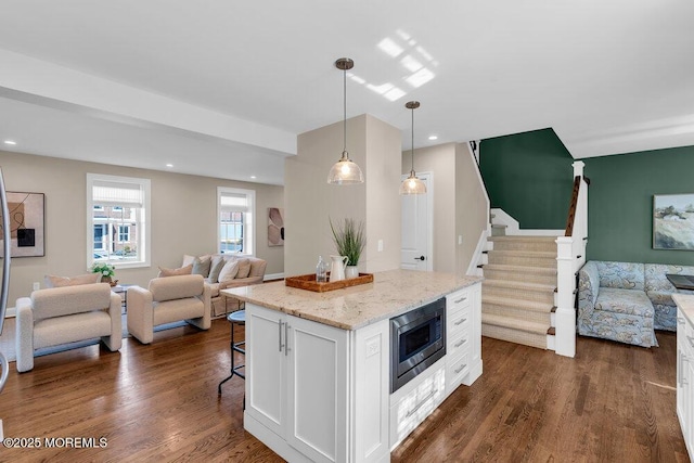 kitchen with dark wood finished floors, white cabinets, open floor plan, stainless steel microwave, and a kitchen bar