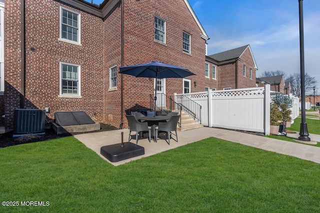 back of house featuring brick siding, fence, a lawn, and central AC unit