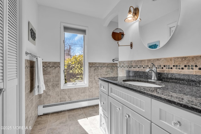 full bathroom featuring tile walls, wainscoting, tile patterned flooring, baseboard heating, and vanity