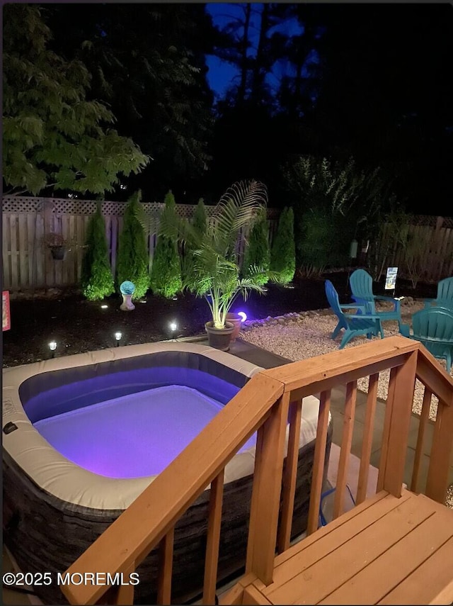 pool at twilight with an outdoor hot tub, fence, and a wooden deck