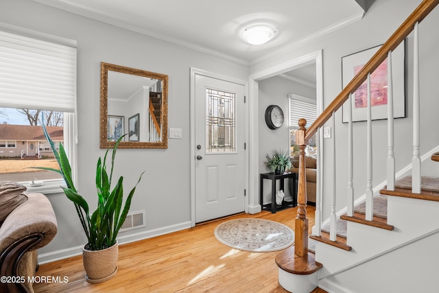 foyer entrance with wood finished floors, visible vents, baseboards, ornamental molding, and stairway