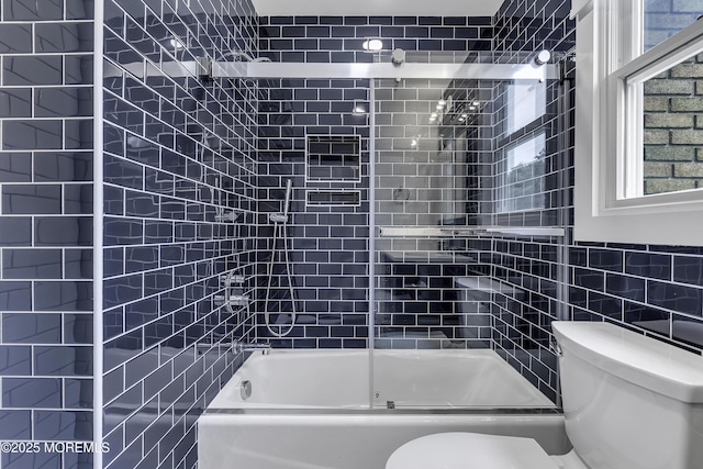 bathroom featuring toilet, combined bath / shower with glass door, and tile walls