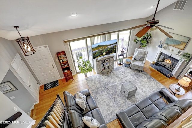 living room featuring lofted ceiling, ceiling fan with notable chandelier, and light hardwood / wood-style flooring