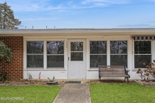 entrance to property featuring a yard, brick siding, and roof with shingles