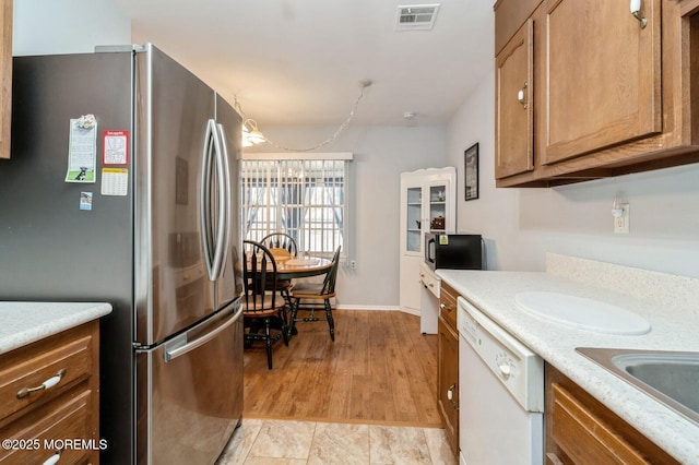 kitchen with light countertops, visible vents, brown cabinetry, freestanding refrigerator, and white dishwasher