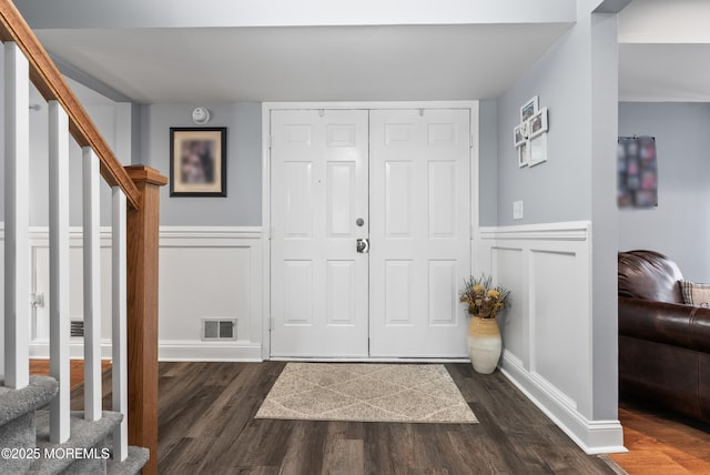 entrance foyer featuring dark wood-style floors, a wainscoted wall, visible vents, and stairs