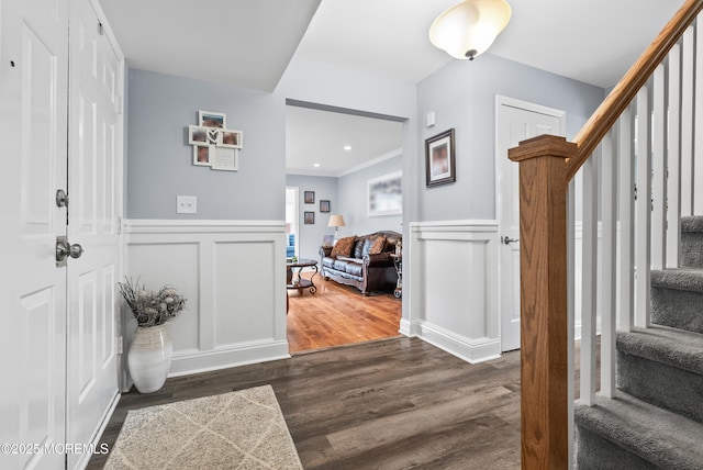 entryway featuring a decorative wall, dark wood-style flooring, ornamental molding, stairway, and wainscoting