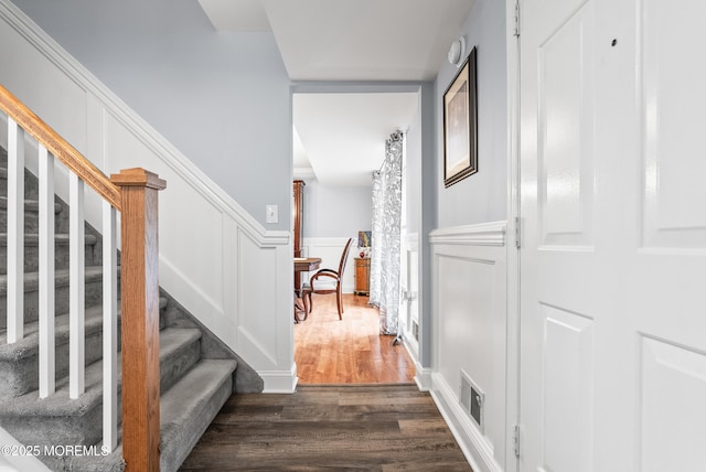 stairway featuring visible vents, a decorative wall, wood finished floors, and wainscoting