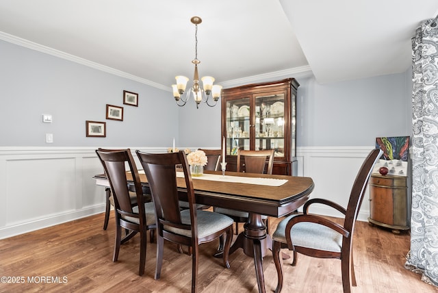 dining room with a chandelier, ornamental molding, wainscoting, and light wood-style flooring