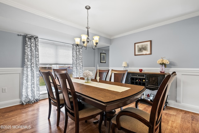 dining room with a wainscoted wall, ornamental molding, wood finished floors, and an inviting chandelier