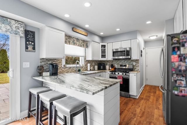 kitchen with dark wood finished floors, appliances with stainless steel finishes, a sink, a peninsula, and a kitchen breakfast bar