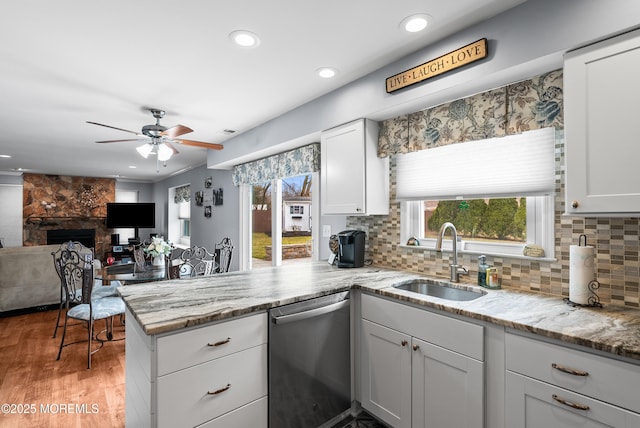 kitchen featuring a peninsula, stainless steel dishwasher, a sink, and tasteful backsplash