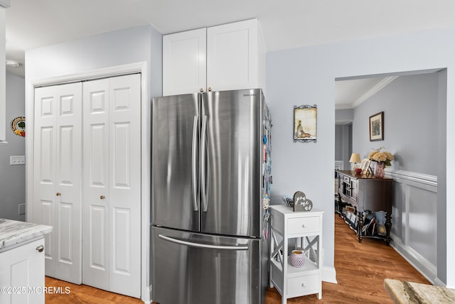 kitchen featuring light stone counters, light wood-style flooring, white cabinetry, ornamental molding, and freestanding refrigerator