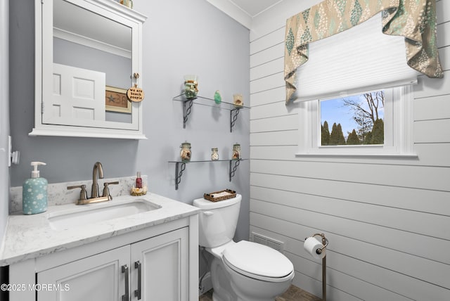 half bathroom with visible vents, wood walls, vanity, and toilet