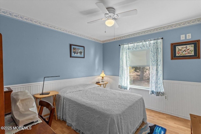 bedroom featuring light wood-style flooring, ceiling fan, and wainscoting