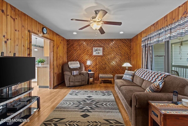 living area with ceiling fan, light wood-style flooring, and wooden walls