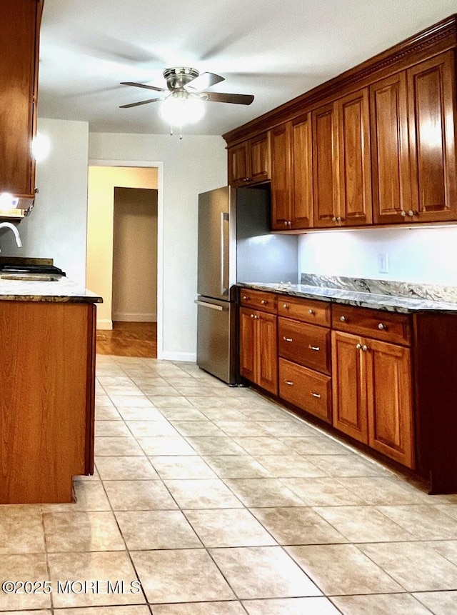 kitchen with ceiling fan, sink, stainless steel fridge, and stone countertops