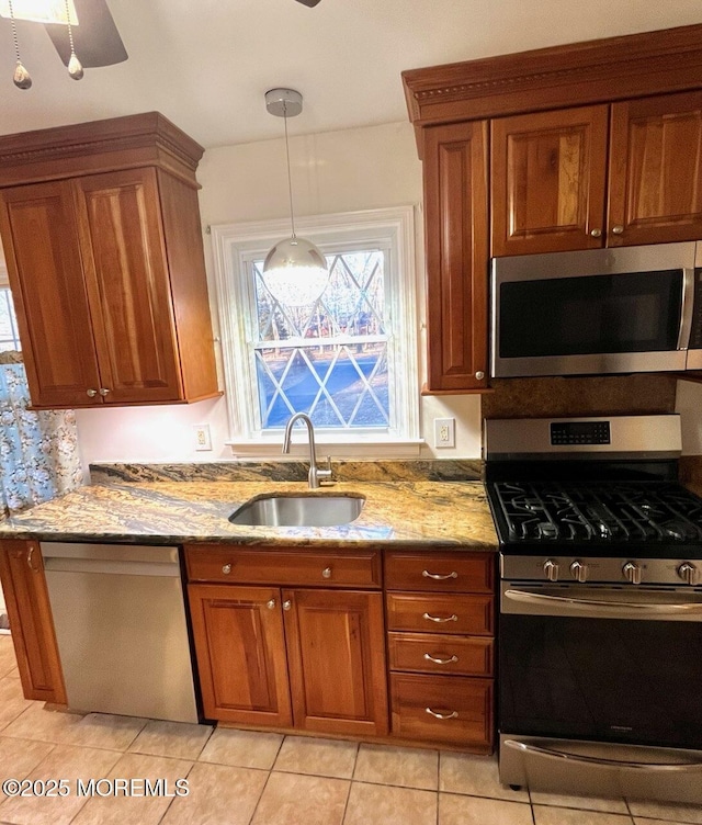 kitchen with sink, stainless steel appliances, light stone counters, and decorative light fixtures