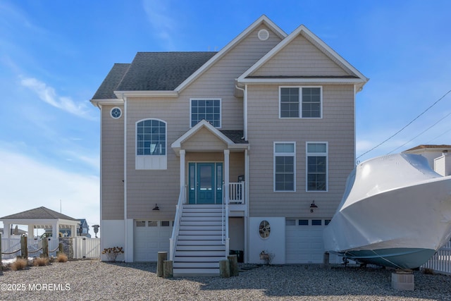 beach home featuring gravel driveway, roof with shingles, fence, and an attached garage