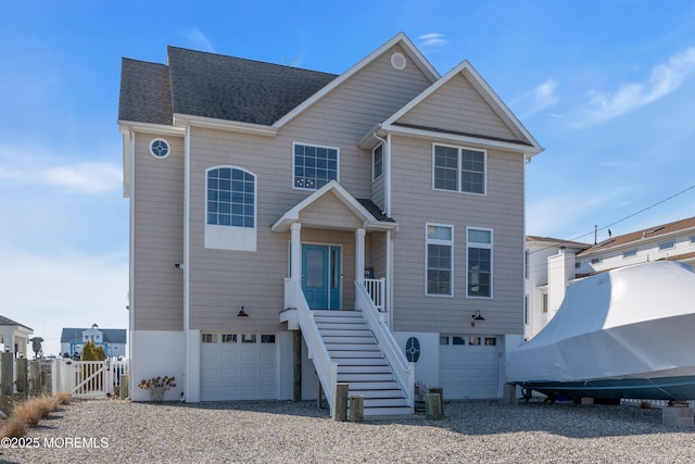 coastal home with a garage, fence, driveway, roof with shingles, and stairway