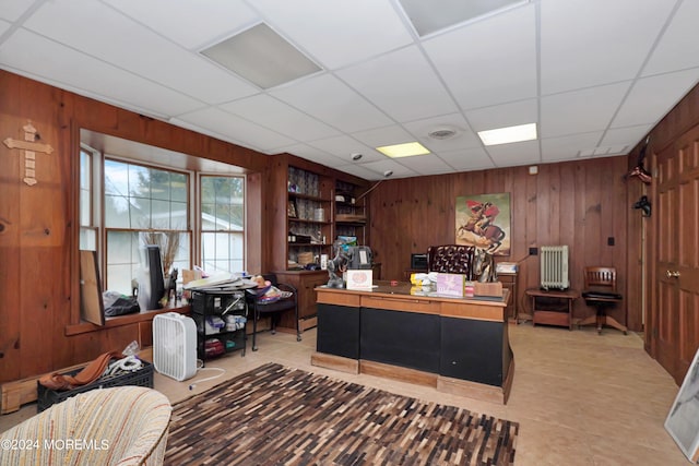 office area featuring wooden walls, a drop ceiling, and radiator