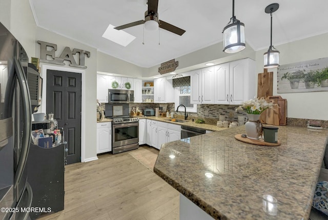 kitchen featuring dark stone countertops, appliances with stainless steel finishes, sink, white cabinets, and hanging light fixtures