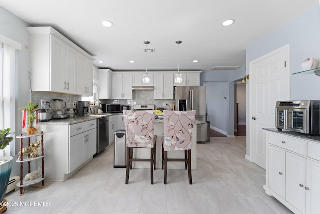 kitchen with pendant lighting, appliances with stainless steel finishes, a center island, light stone countertops, and white cabinets