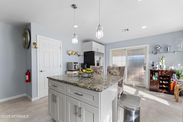 kitchen featuring stainless steel refrigerator with ice dispenser, white cabinetry, decorative light fixtures, a kitchen island, and stone counters