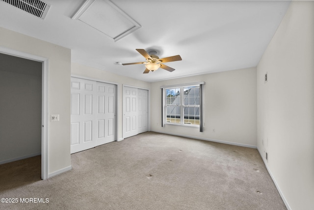 unfurnished bedroom with ceiling fan, multiple closets, and light carpet