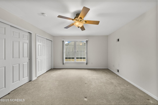 unfurnished bedroom featuring ceiling fan, two closets, and light carpet