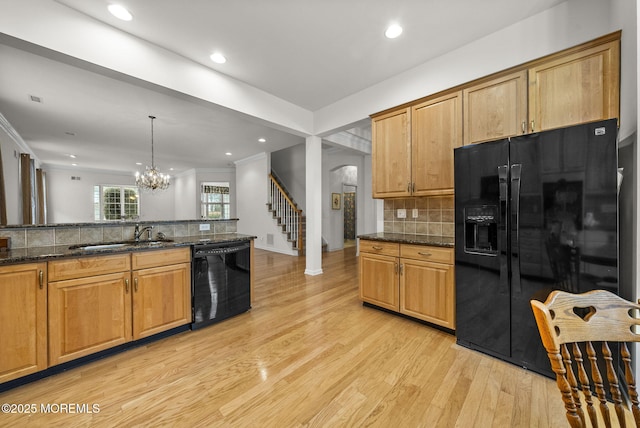 kitchen with dark stone countertops, sink, light wood-type flooring, black appliances, and hanging light fixtures