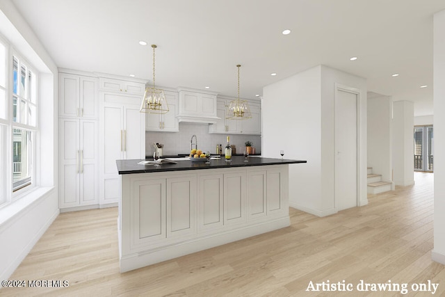 kitchen featuring light wood finished floors, tasteful backsplash, an island with sink, dark countertops, and pendant lighting