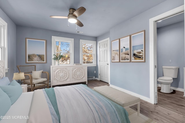 bedroom with ensuite bathroom, light wood-type flooring, baseboard heating, and ceiling fan