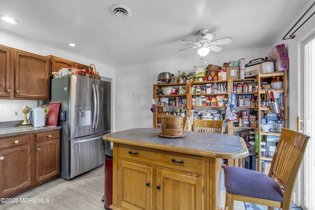 kitchen featuring tile countertops, visible vents, stainless steel fridge with ice dispenser, backsplash, and brown cabinets