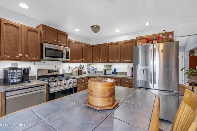 kitchen featuring brown cabinetry, decorative backsplash, tile countertops, appliances with stainless steel finishes, and recessed lighting