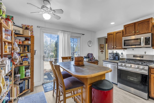 kitchen with appliances with stainless steel finishes, brown cabinets, light wood-style flooring, and tile countertops