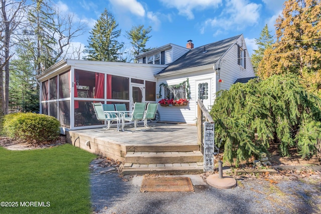 back of house with a sunroom, a chimney, and a lawn