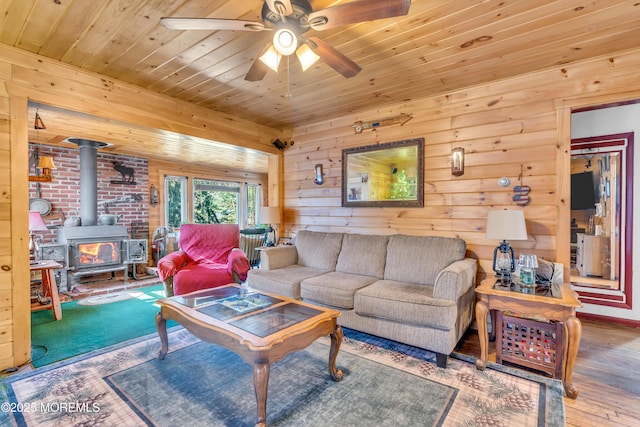 living room with a ceiling fan, wood ceiling, a wood stove, and wood finished floors