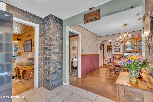 dining space with light tile patterned floors, ornamental molding, wainscoting, a chandelier, and wallpapered walls