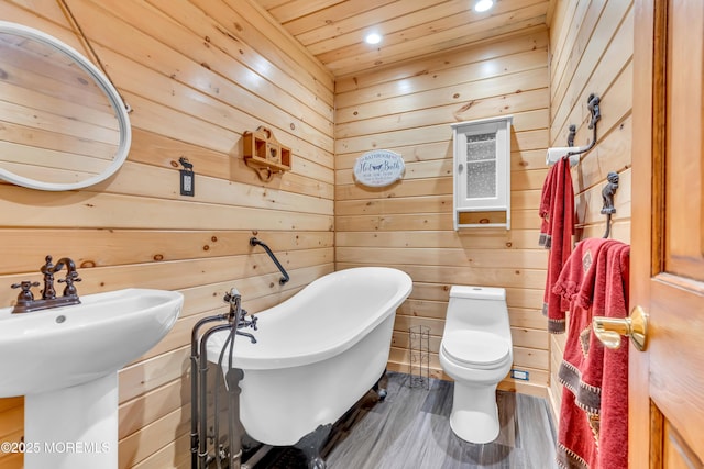 full bathroom with wooden walls, toilet, wood finished floors, a freestanding tub, and recessed lighting